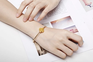 Detail of adjustable gold clover bangle on wrist with a stylish magazine background