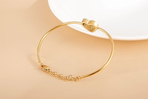 Detail of gold heart bracelet with MOM engraving and adjustable chain on beige background