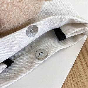 Détail du fermoir magnétique argenté et de la texture en toile d'un sac blanc