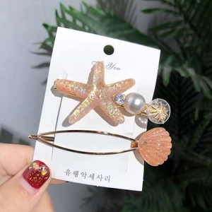 Close-up of starfish and shell hair clips with pearls and rhinestones on green leaves