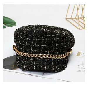 Close-up of black and gold tweed newsboy cap with decorative gold chain and buttons