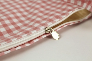 Detail shot of a silver oval zipper on pink and white gingham canvas fabric