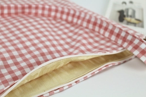Detailed close-up of pink checkered canvas bag featuring white zipper and yellow lining