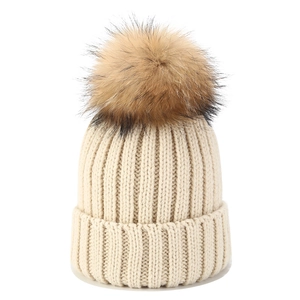 Detail einer beigen Strickmütze mit grober Rippstruktur und flauschigem braunem Bommel