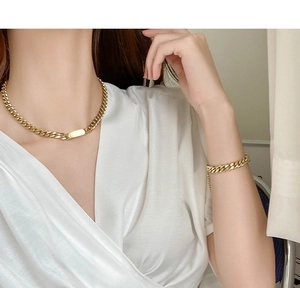 Close-up of gold cuban chain necklace and bracelet set with rectangular tag on model