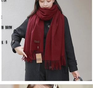 Close-up of a burgundy cashmere scarf with a leather logo patch and tassel fringe detail