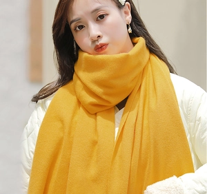 Detailed close-up of soft yellow cashmere knit scarf texture and elegant fringe on model