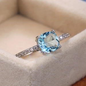 Macro shot of a square blue zircon ring with diamond side stones on a beige velvet box