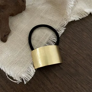 Close-up of golden brushed metal hair tie on a rustic background with wood and linen