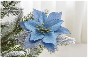 Close-up of blue glitter artificial poinsettia flower on snowy Christmas tree branches