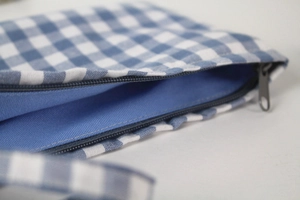 Detail view of the blue checkered cotton fabric and grey zipper on the storage pouch