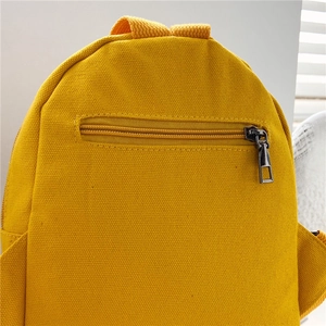 Detail of yellow canvas backpack showing the zipper pocket and top handle texture