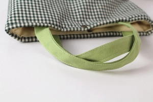 Detail of green plaid canvas tote bag showing metal snap button and sturdy handle
