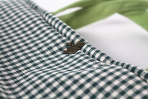 Macro shot of green checkered canvas bag showing detailed stitching and vintage metal button
