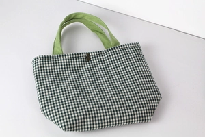 Detail of green gingham canvas tote bag with bright green straps and bear ornament