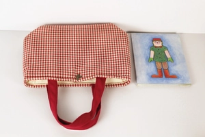 Macro detail of red gingham canvas tote bag featuring bronze pendant and red handles