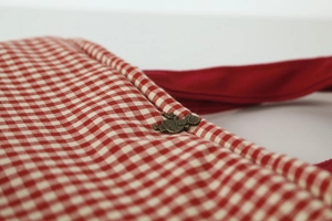 Detail of red gingham cotton bag with vintage bronze figurine charm and stitch texture