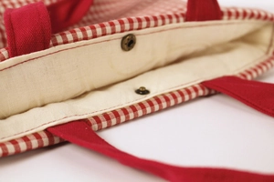 Close-up of red and white plaid canvas tote bag with metal snap button and cotton lining