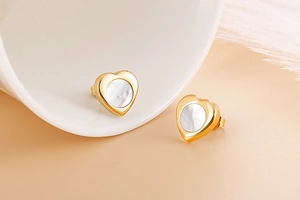 Detail view of heart-shaped gold earrings with inlaid white mother-of-pearl center