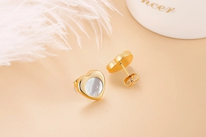 Detail of heart-shaped gold earrings with white mother of pearl inlay and stud closure