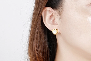 Detailed view of heart-shaped shell earrings in gold on ear model for size reference