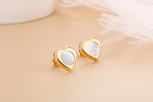 Macro shot of heart-shaped gold stud earrings featuring elegant white shell inlay details