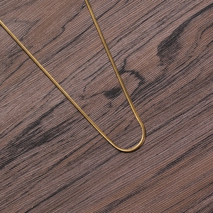 Detail view of 2mm golden stainless steel snake chain on dark wood background texture