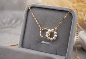 Close-up of interlocking gold rings with freshwater pearls on grey velvet jewelry box