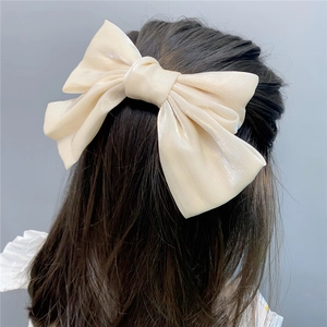 Close-up of a large cream satin bow hair clip on a woman's half-up hairstyle