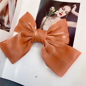 Close-up of elegant orange organza bow hair clip with metallic sheen on a fashion magazine