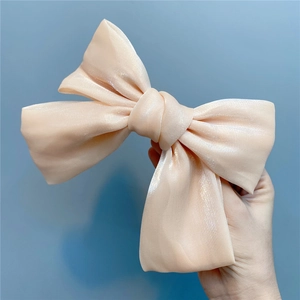 Detail of a champagne organza bow hair clip with glossy silk texture and metal spring