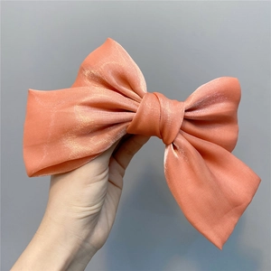 Macro view of a coral pink organza bow hair clip featuring a high-gloss silk texture