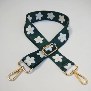 Detail of wide nylon shoulder strap with white daisy print and golden metal buckles