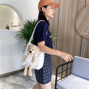 Détail d'un sac cabas en toile blanche avec un ours en peluche 3D porté par un mannequin