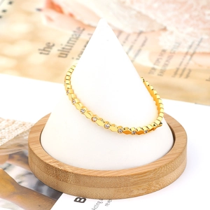 Detail of a geometric hexagonal golden bracelet with inlaid cubic zirconia on a white stand