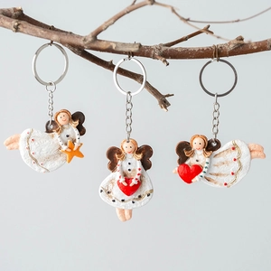 Three creative Christmas angel keychains with red hearts and yellow stars on tree branch