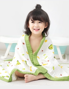 Close-up of baby in cotton gauze towel with avocado print next to a bathtub