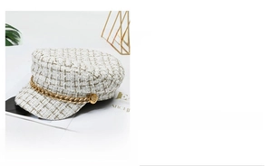 Detail of white tweed baker boy hat featuring a decorative gold chain and metal button