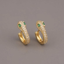 Close-up of snake-shaped golden earrings with white zircon pavé and green gem eyes