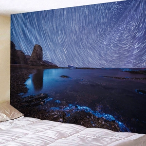 Deep blue starry night beach tapestry hanging above a bed in a cozy bedroom setting