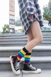 Detail of colorful rainbow striped high socks worn with casual sneakers on a stone step