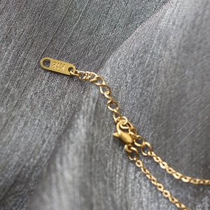 Macro detail of 18K gold-plated lobster clasp and extension chain with K18 engraved tag