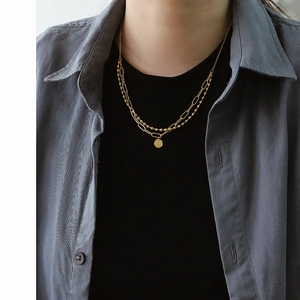 Detail of double-layer golden paperclip and bead necklace with a round pendant on a model