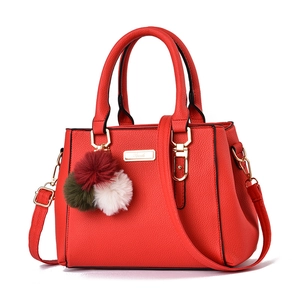 Minimalist red leather handbag with top handles, gold hardware, and colorful pompom