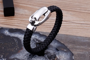 Macro detail of a silver lion head charm on a black braided leather bracelet over stones