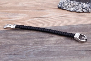 Detail of black braided leather bracelet with silver skull clasp on a wooden background