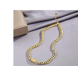 Detailed view of a gold cuban link necklace with a rectangular plate on grey silk fabric
