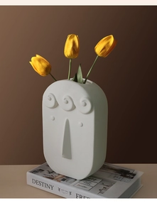 Detail of a white ceramic face vase with matte finish and yellow tulips on a book