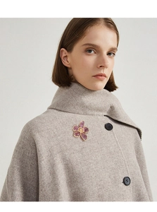 Detail of a purple crystal flower brooch with gold edges on a grey wool coat lapel