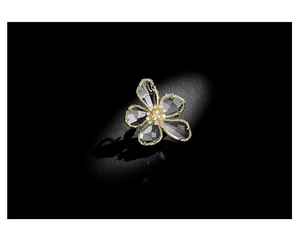Macro detail of crystal flower brooch with gold edges and zircon center on black background